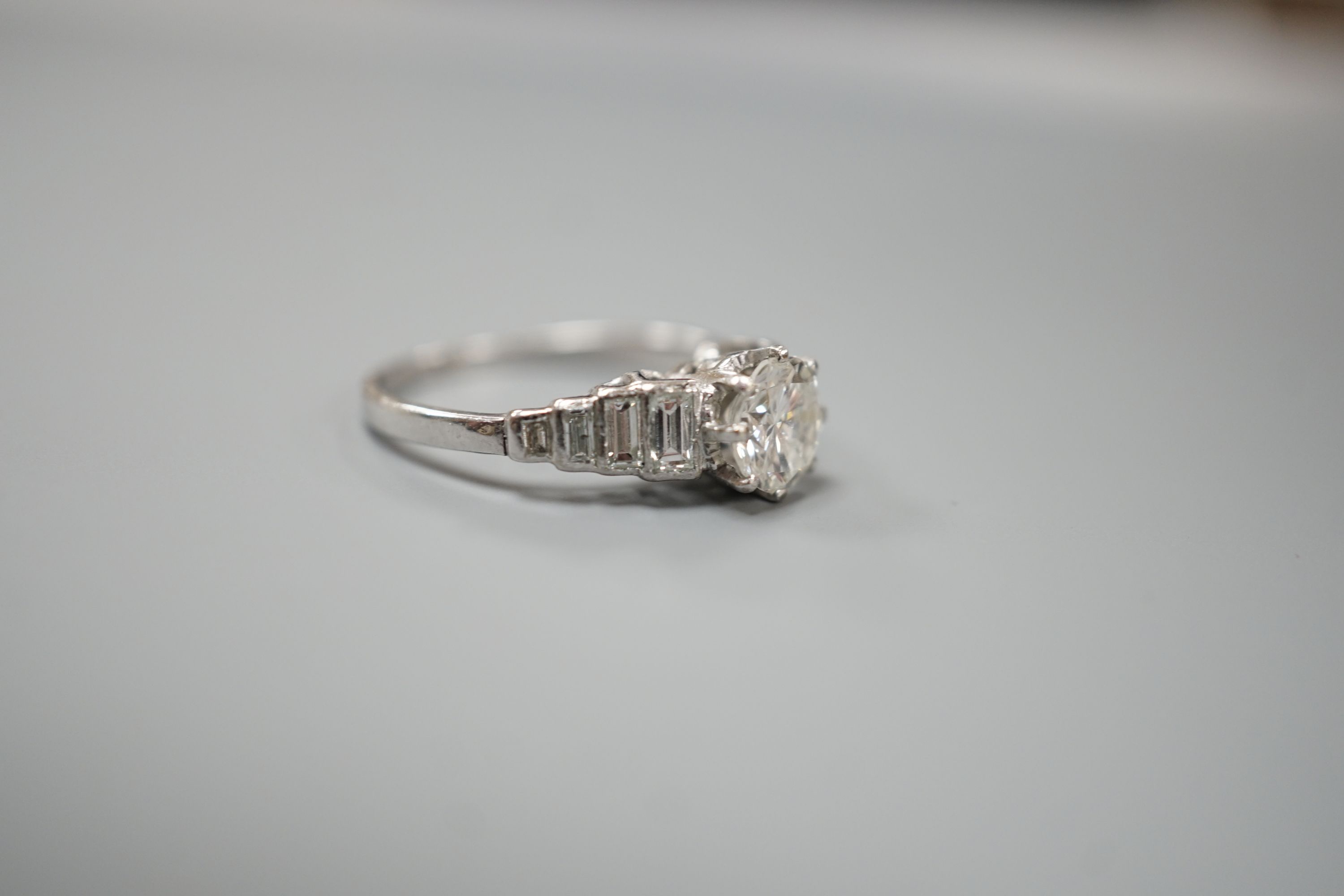 A white metal (stamped Plat) and single stone diamond ring, with graduated eight stone baguette cut diamond set shoulders, size K/L, gross weight 3.5 grams